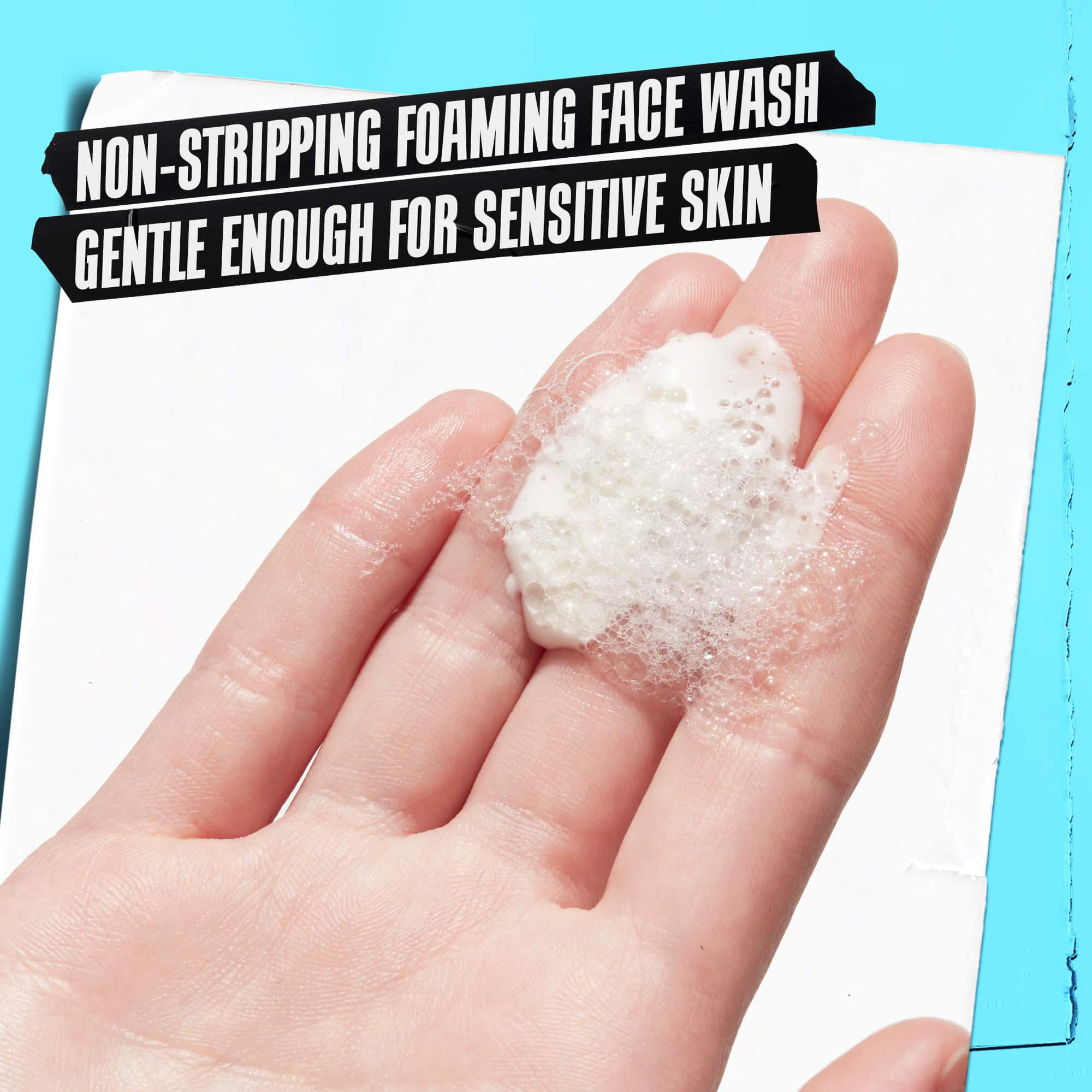 Una mano che tiene la schiuma di Ultra Facial Oil-Free Cleanser etichettata "Detergente schiumogeno non aggressivo, abbastanza delicato per pelli sensibili."