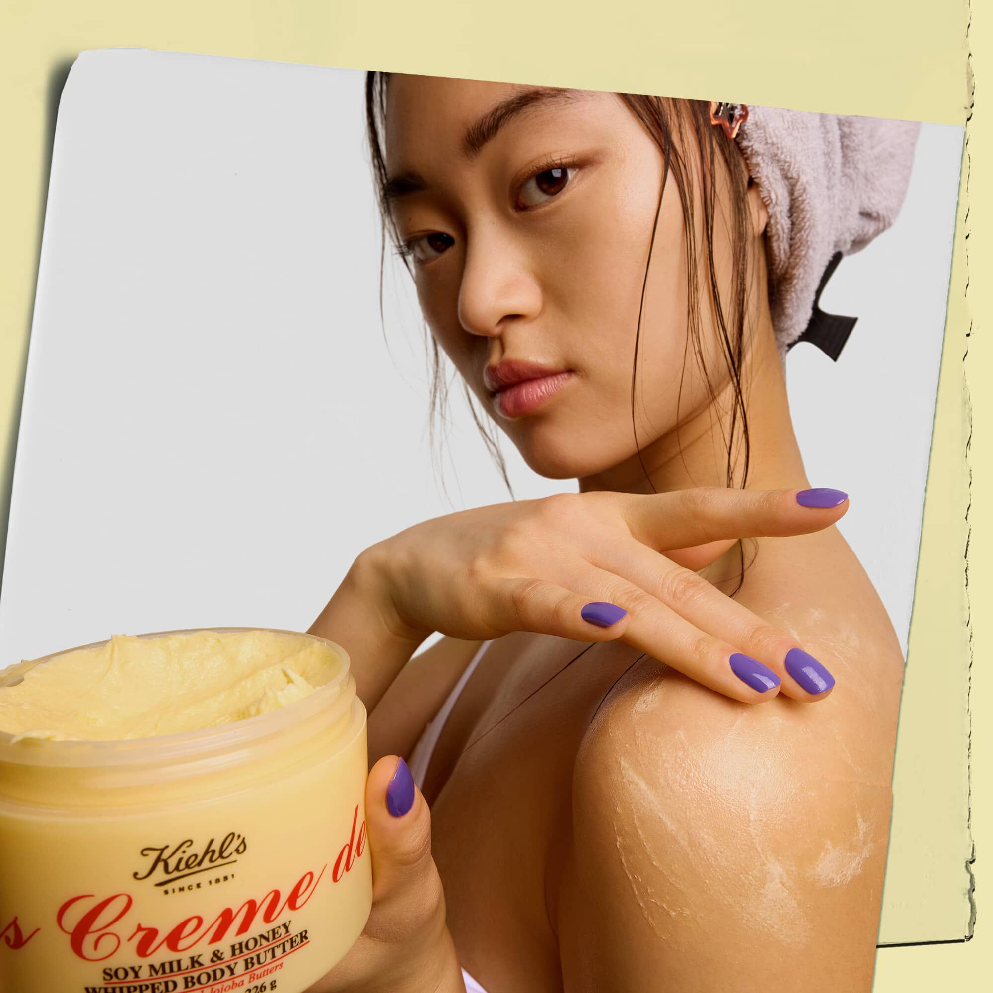Modella con in mano un vasetto mentre applica il burro per il corpo Kiehl's Creme de Corps Whipped Butter