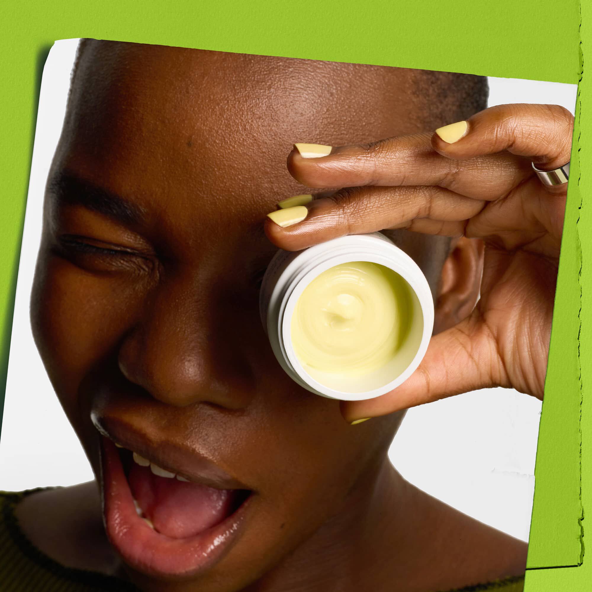 Modella che fa l'occhiolino con un vasetto di Kiehl's Creamy Eye Treatment with Avocado che copre un occhio